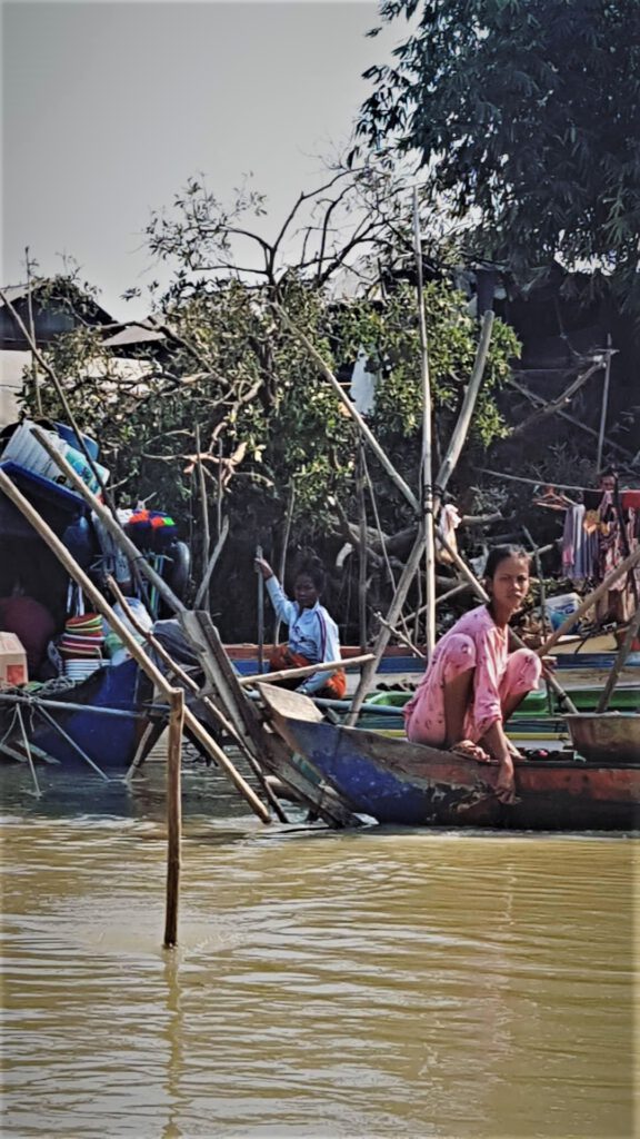 Junge Kambodschanerin in einem pinken Pyjama in der asiatischen Hocke auf einem Bott während sie im Fluss Wäsche wascht