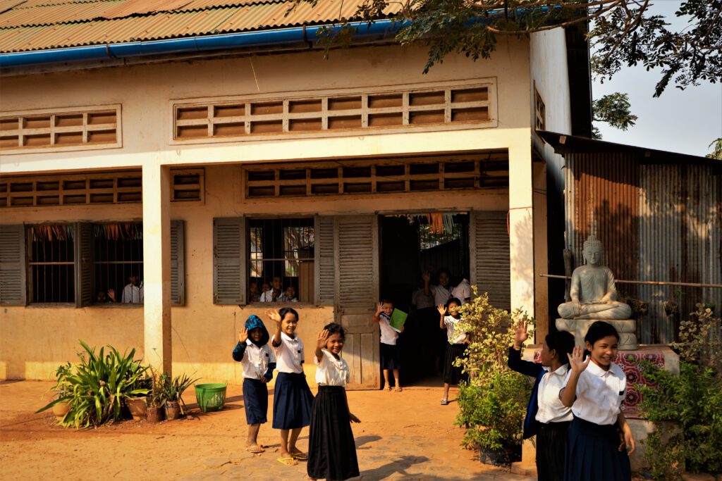 Kambodschanische Schulmädchen stürmen aus dem Unterricht und winken