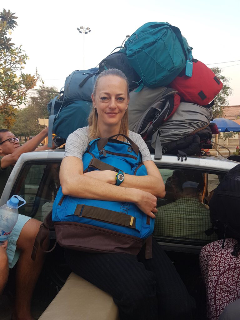 Blonde Frau mit blauem Rucksack und viel Gepäck im Hintergrund auf einem Pick Up in Battambang Kambodscha
